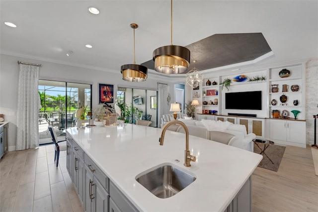 kitchen featuring ornamental molding, open floor plan, gray cabinets, built in shelves, and a sink