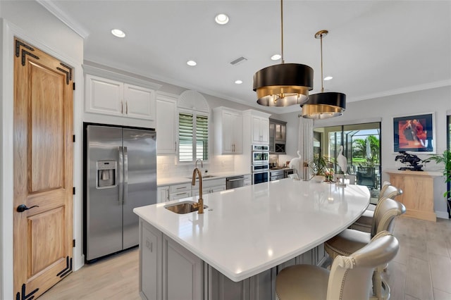 kitchen with a large island, stainless steel appliances, light countertops, ornamental molding, and a sink