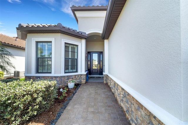 property entrance with stone siding, a tile roof, cooling unit, and stucco siding