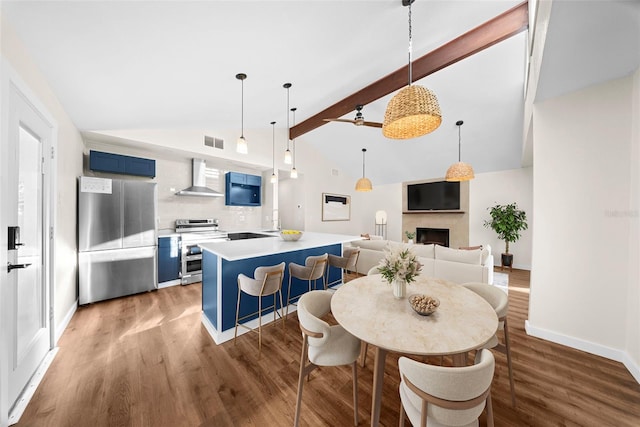 dining room featuring vaulted ceiling with beams, a fireplace, visible vents, wood finished floors, and baseboards