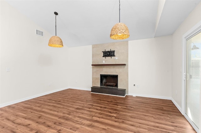 unfurnished living room featuring a tile fireplace, visible vents, baseboards, and wood finished floors