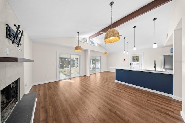 unfurnished living room with vaulted ceiling with beams, plenty of natural light, a tiled fireplace, and wood finished floors