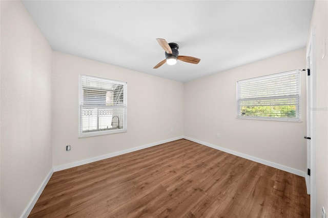 spare room featuring a ceiling fan, a wealth of natural light, baseboards, and wood finished floors