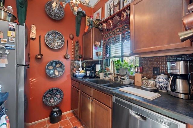 kitchen featuring a sink, appliances with stainless steel finishes, backsplash, brown cabinets, and dark countertops