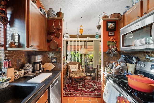 kitchen featuring dark countertops, appliances with stainless steel finishes, brown cabinets, a textured ceiling, and backsplash