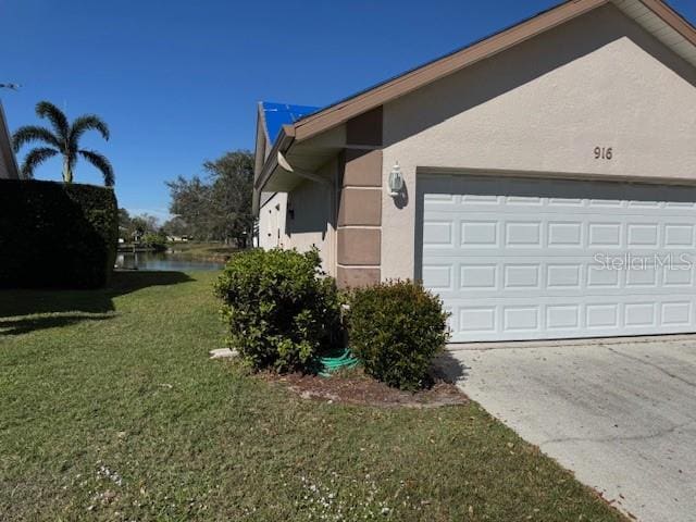 view of side of home with driveway, a garage, a lawn, a water view, and stucco siding