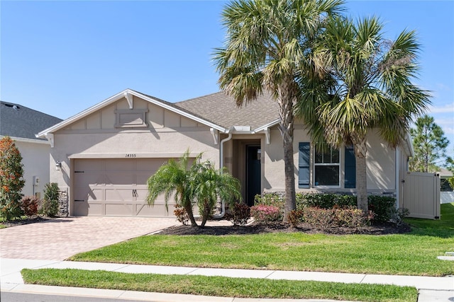 ranch-style house featuring a shingled roof, stucco siding, an attached garage, decorative driveway, and a front yard