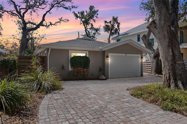 view of front of home featuring decorative driveway, an attached garage, fence, and stucco siding