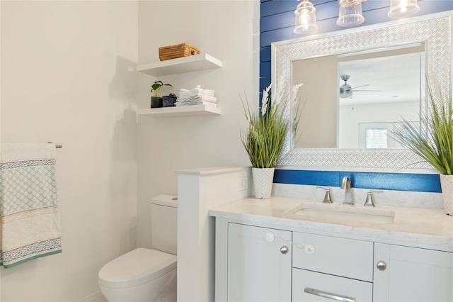 half bathroom with ceiling fan, vanity, and toilet