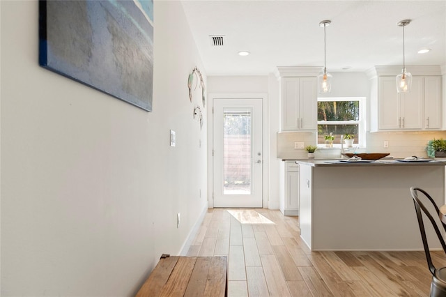 kitchen featuring visible vents, white cabinets, light wood-type flooring, backsplash, and pendant lighting