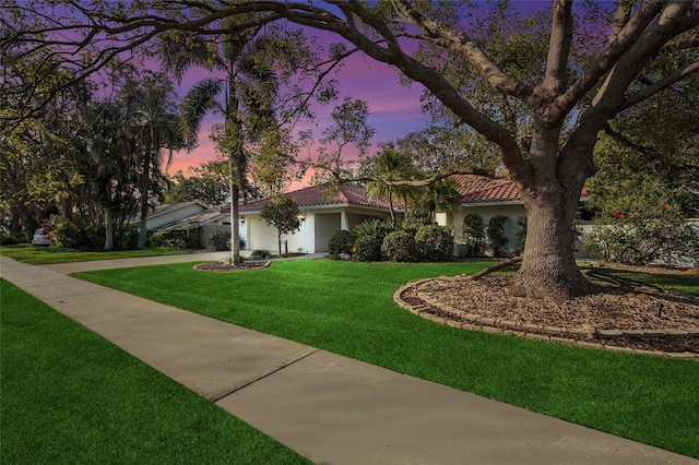 view of front of home featuring an attached garage, a tile roof, concrete driveway, a yard, and stucco siding