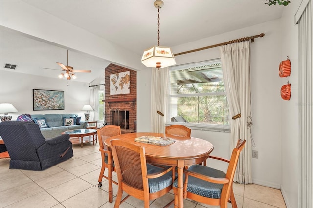 dining space with visible vents, a ceiling fan, vaulted ceiling, a brick fireplace, and light tile patterned flooring