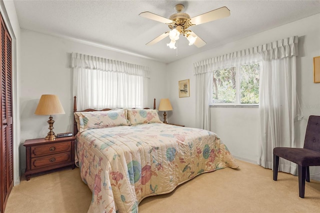 bedroom featuring a ceiling fan, a closet, light carpet, and a textured ceiling