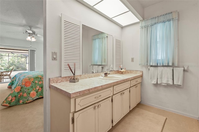 ensuite bathroom with a skylight, vanity, baseboards, a ceiling fan, and ensuite bath