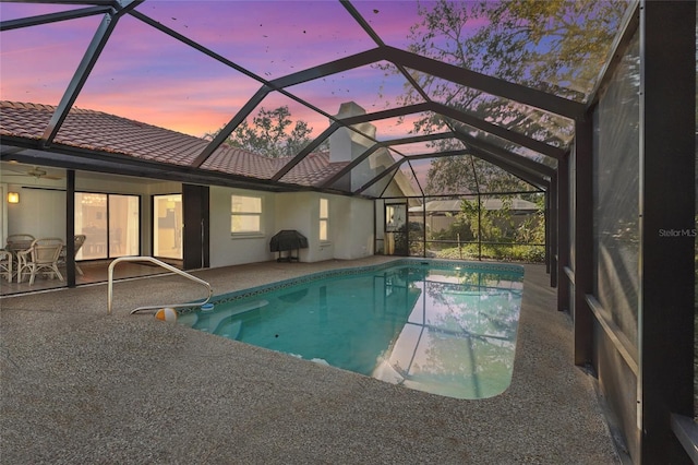 pool at dusk featuring an outdoor pool, a lanai, and a patio