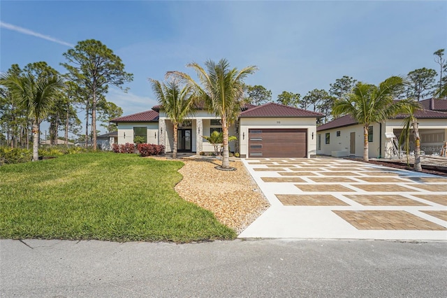 mediterranean / spanish home with decorative driveway, a tile roof, stucco siding, an attached garage, and a front yard