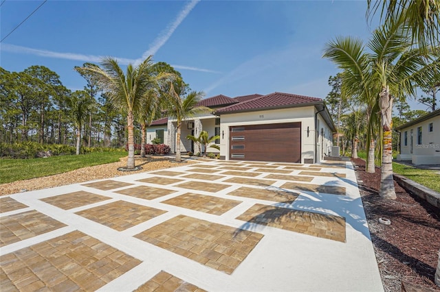 mediterranean / spanish house featuring a garage, a tiled roof, decorative driveway, and stucco siding