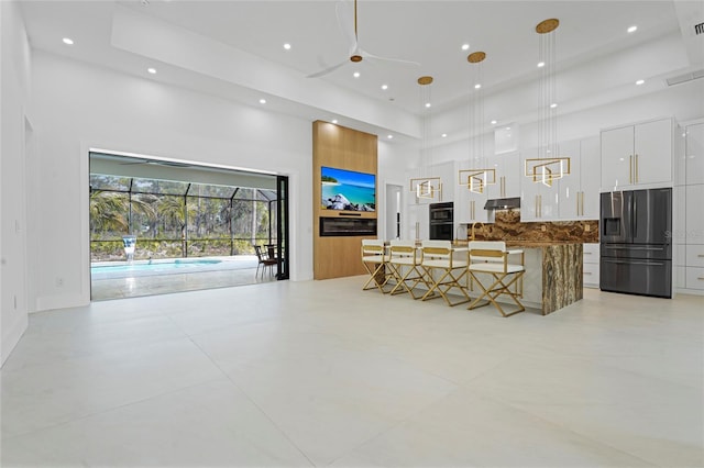 living room with a towering ceiling, ceiling fan, a raised ceiling, and recessed lighting