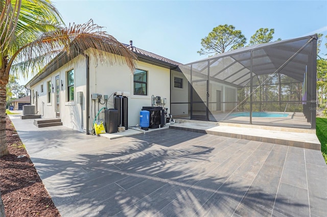 rear view of property with an outdoor pool, glass enclosure, a patio area, central AC, and stucco siding