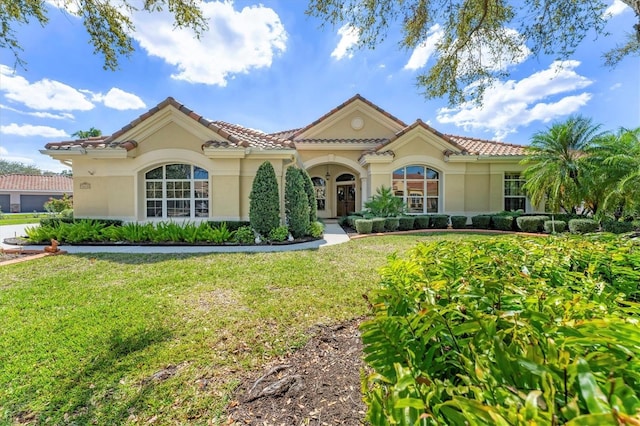 mediterranean / spanish home with a tiled roof, a front lawn, and stucco siding