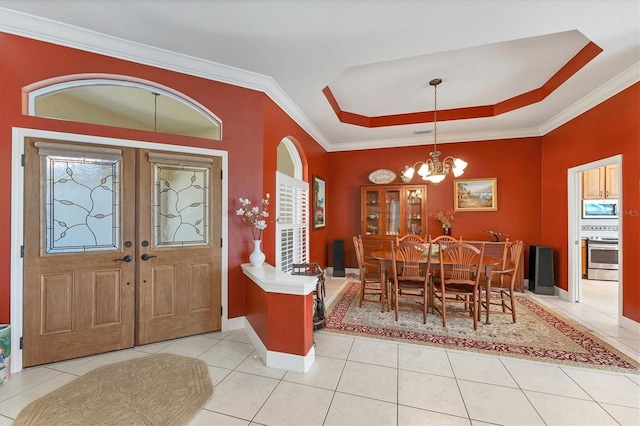 foyer entrance with ornamental molding, a raised ceiling, a notable chandelier, and light tile patterned floors