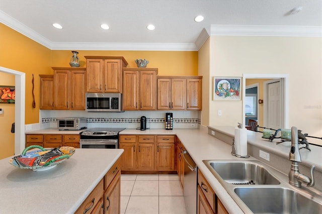 kitchen with stainless steel appliances, a sink, light countertops, brown cabinetry, and crown molding