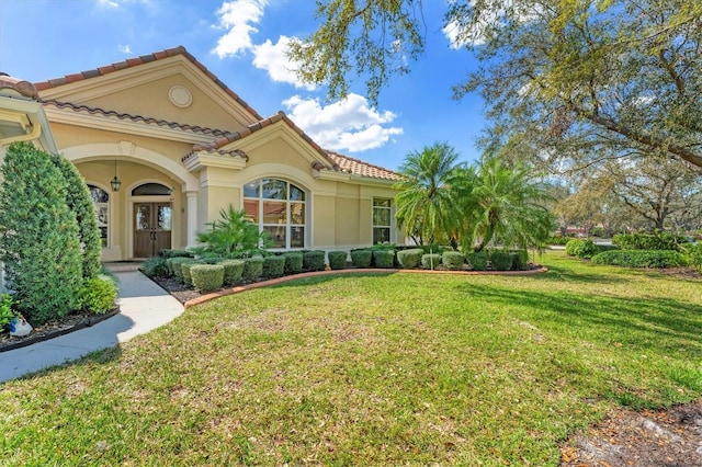 mediterranean / spanish-style house featuring a front yard, a tile roof, and stucco siding