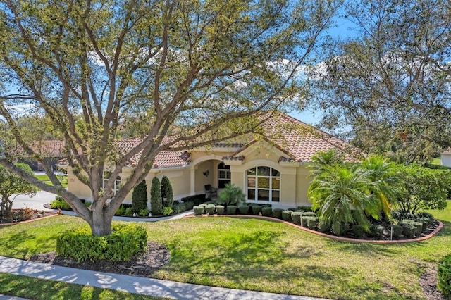 mediterranean / spanish house with a front yard, a tiled roof, and stucco siding