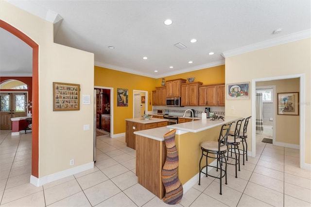 9612 Old Hyde Park Pl, Bradenton, FL 34202 - kitchen featuring appliances with stainless steel finishes, a peninsula, a kitchen bar, light tile patterned flooring, and crown molding