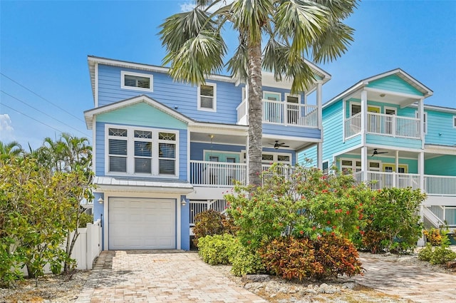 coastal home with a garage, ceiling fan, fence, and decorative driveway