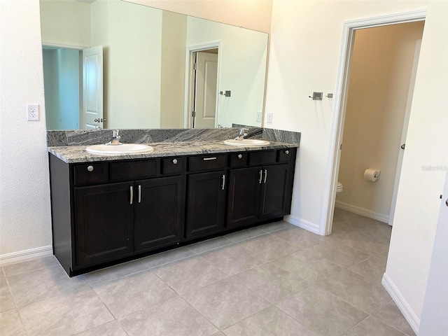 full bath featuring double vanity, baseboards, toilet, and a sink