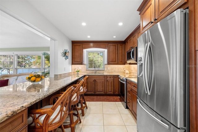 kitchen featuring light tile patterned floors, light stone counters, appliances with stainless steel finishes, a kitchen breakfast bar, and a sink