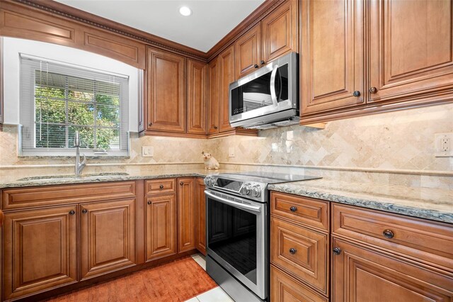 kitchen featuring brown cabinetry, light stone counters, stainless steel appliances, and a sink