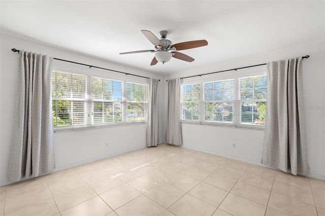 empty room with light tile patterned floors, ceiling fan, baseboards, and a wealth of natural light