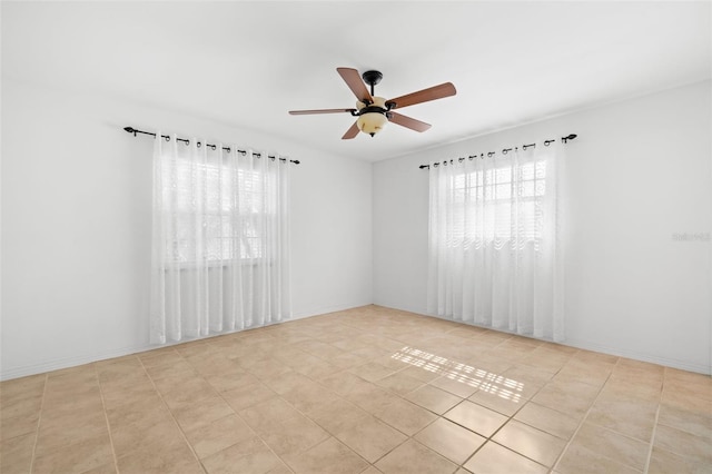 tiled empty room with ceiling fan and baseboards