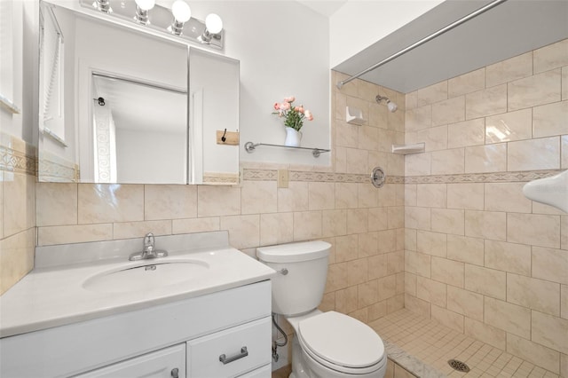 full bathroom with toilet, a tile shower, vanity, and tile walls