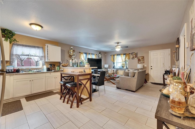 kitchen featuring white cabinets, ceiling fan, open floor plan, a textured ceiling, and a sink