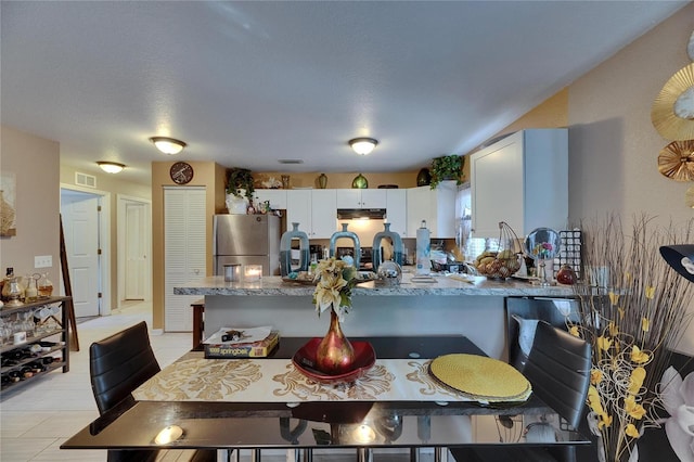 kitchen with under cabinet range hood, a peninsula, visible vents, white cabinetry, and freestanding refrigerator