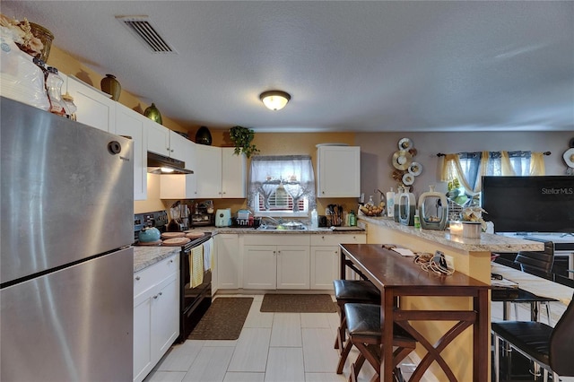 kitchen featuring under cabinet range hood, a sink, visible vents, black electric range, and freestanding refrigerator