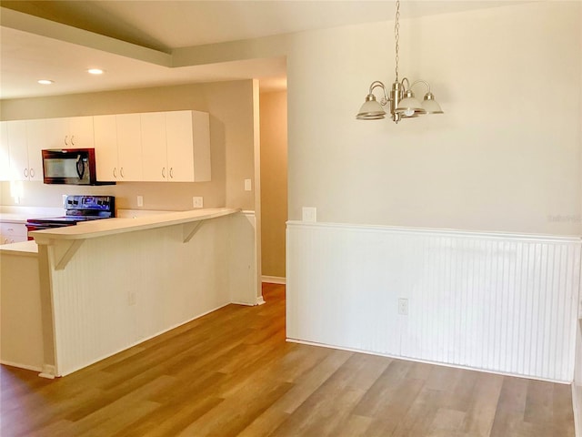 kitchen with black microwave, range with electric cooktop, a kitchen breakfast bar, light countertops, and light wood-type flooring