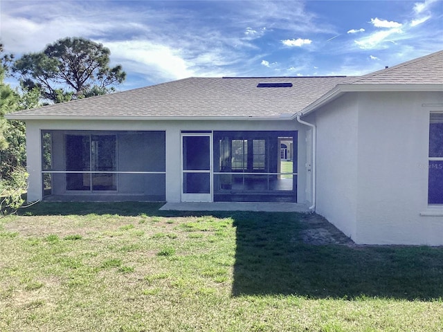 rear view of house featuring a yard, a shingled roof, a sunroom, and stucco siding