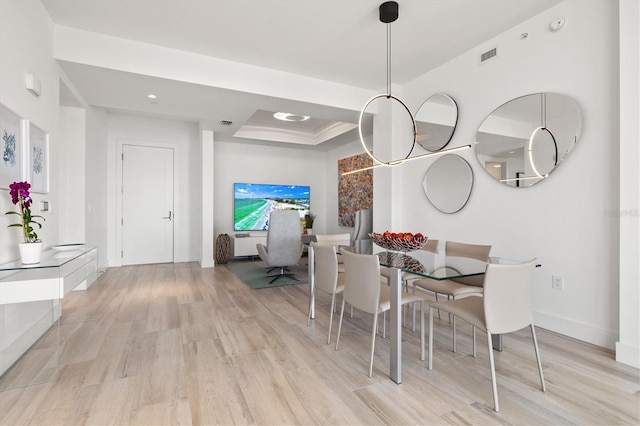 dining room featuring light wood finished floors, visible vents, a tray ceiling, and baseboards