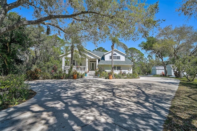 view of front of property with a porch, an outdoor structure, driveway, and a shed