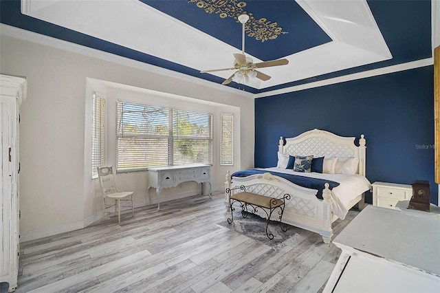 bedroom featuring crown molding, baseboards, wood finished floors, a raised ceiling, and a ceiling fan