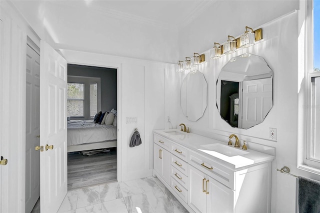 ensuite bathroom with crown molding, double vanity, marble finish floor, and a sink