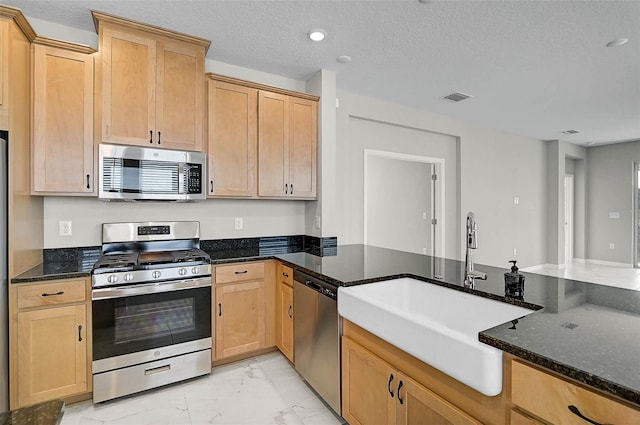 kitchen with a sink, dark stone counters, marble finish floor, and stainless steel appliances