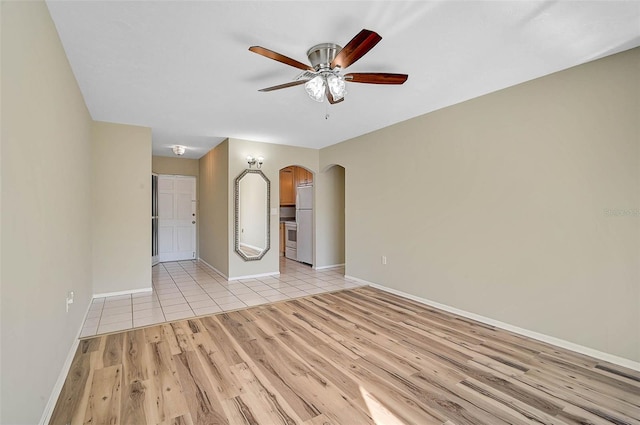 unfurnished room featuring light wood-style flooring, a ceiling fan, arched walkways, and baseboards