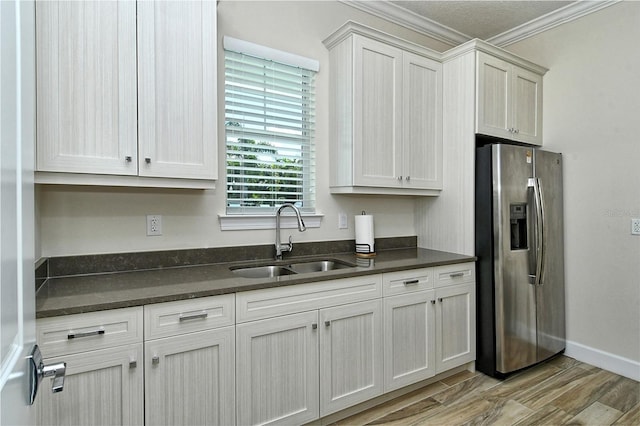 kitchen with crown molding, stainless steel refrigerator with ice dispenser, light wood-style floors, a sink, and baseboards