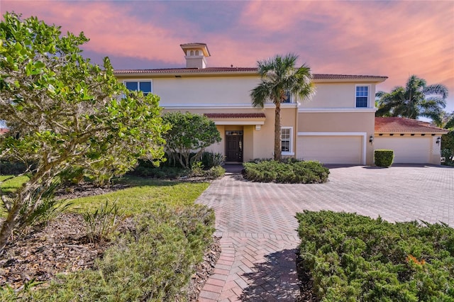 mediterranean / spanish-style home featuring a tiled roof, decorative driveway, a garage, and stucco siding