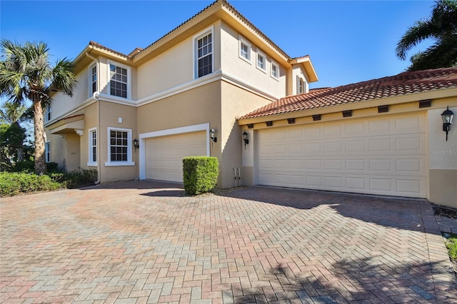 mediterranean / spanish house featuring a tiled roof, decorative driveway, a garage, and stucco siding